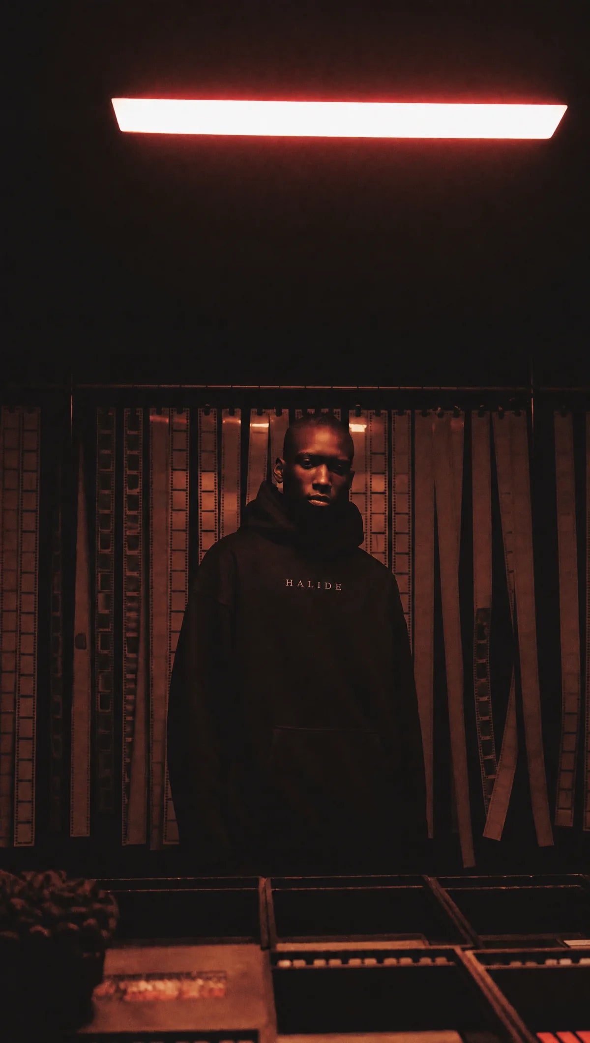 A man in a black heavyweight hoodie in a darkroom under red safelight.