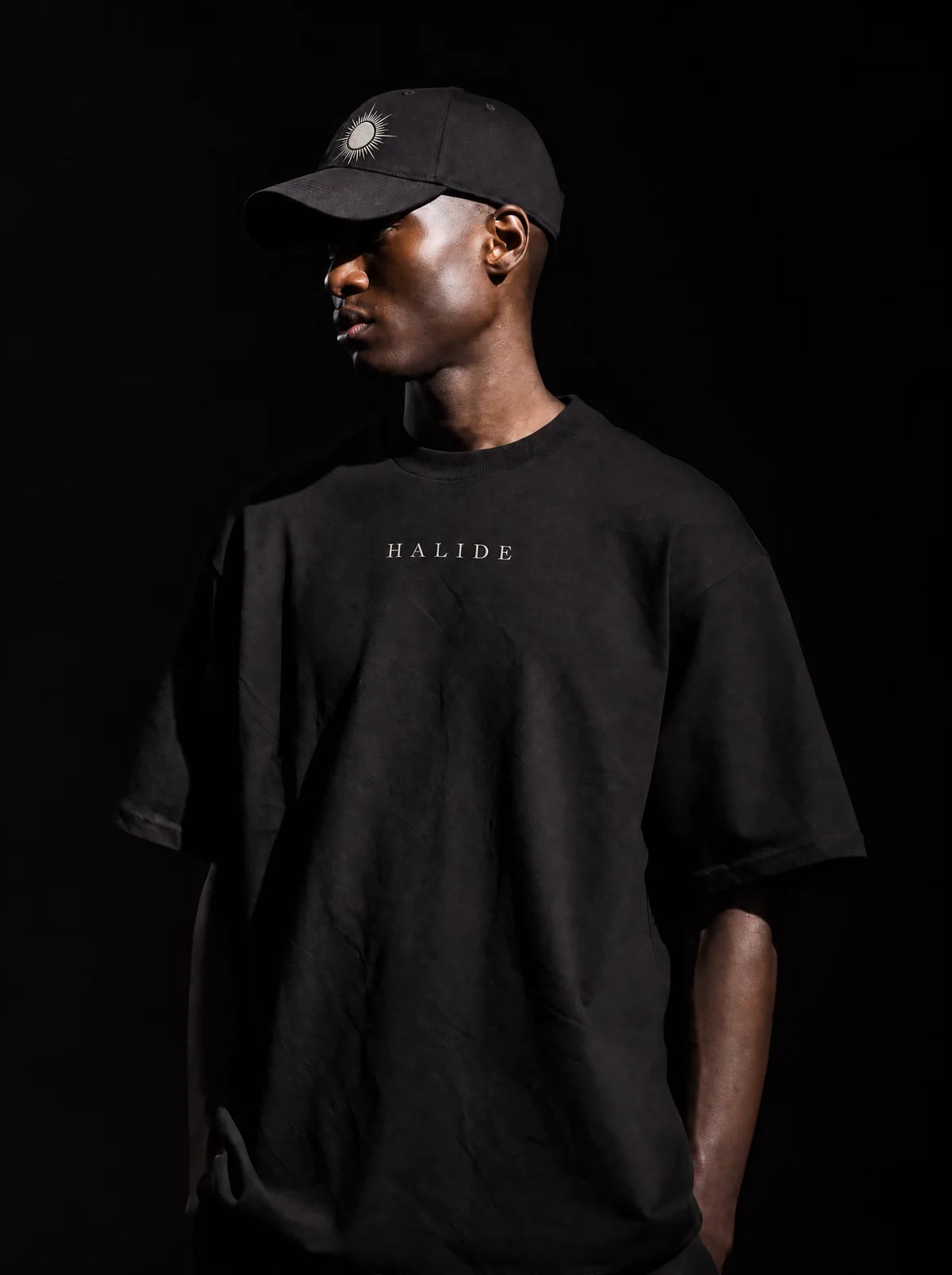 A man in a black cap and tee lit from the side against black.