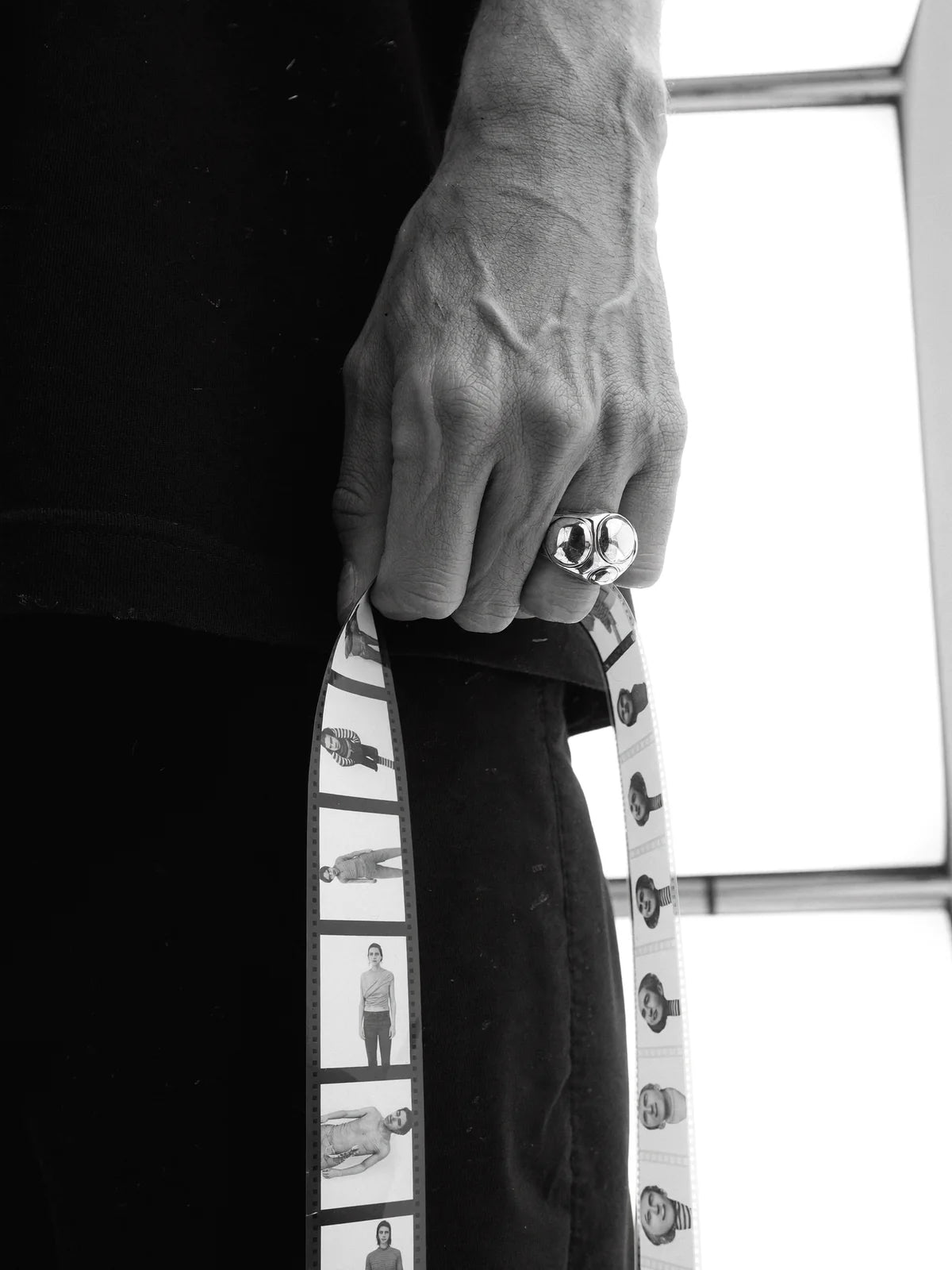 A hand with a signet ring holding a strip of film negatives to the light.